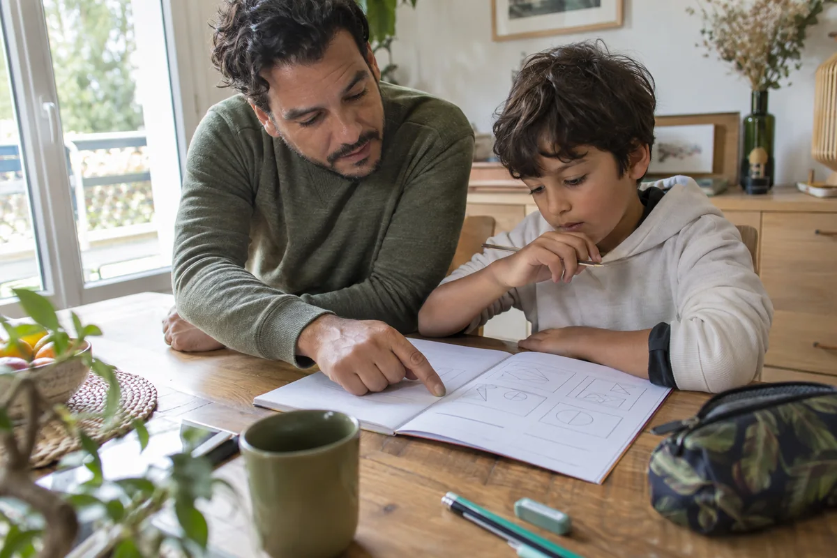Un père accompagne son fils pendant un exercice dans un cahier.