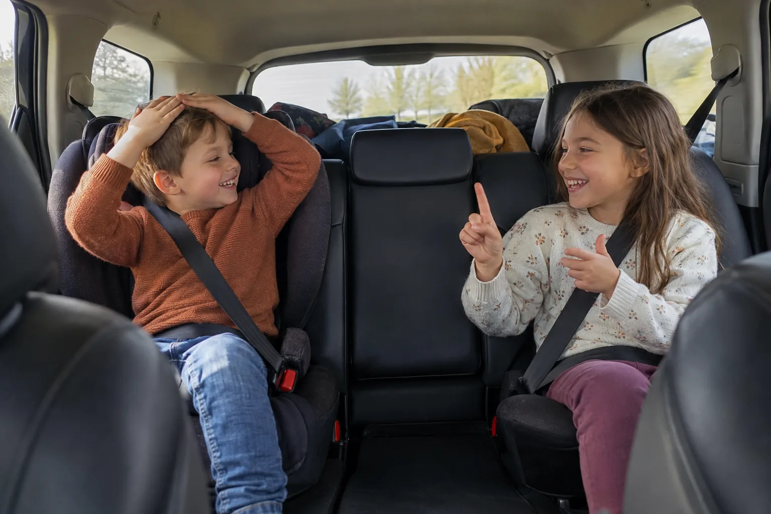 À l’arrière d’une voiture, deux enfants bien attachés dans leurs sièges jouent à un jeu de devinettes en riant.