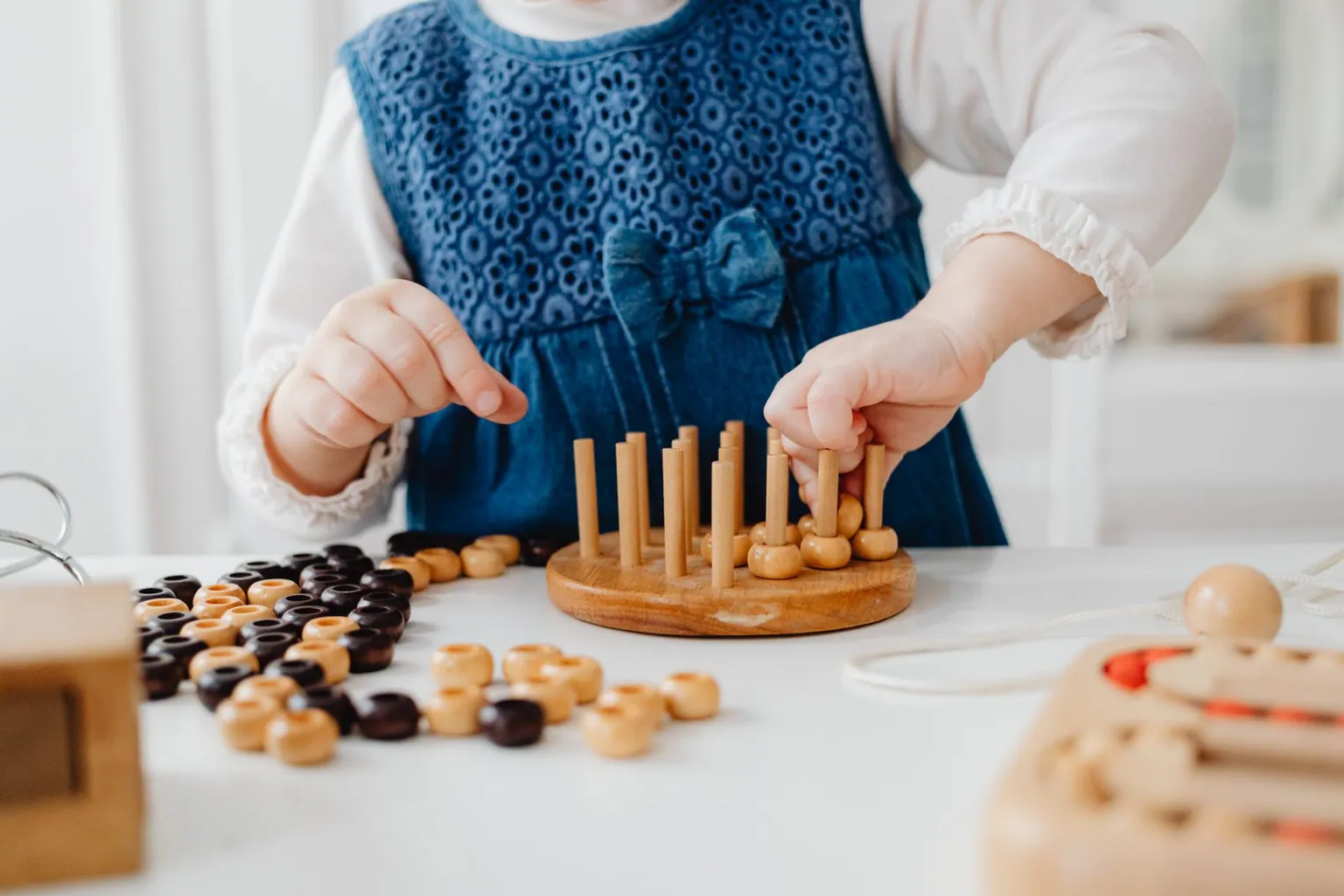 Une enfant enfile des perles en bois sur des tiges posées sur une table.