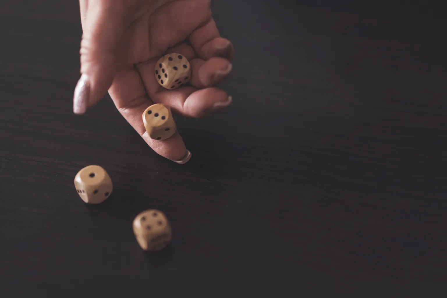 Une main lance des dés en bois sur une table sombre.