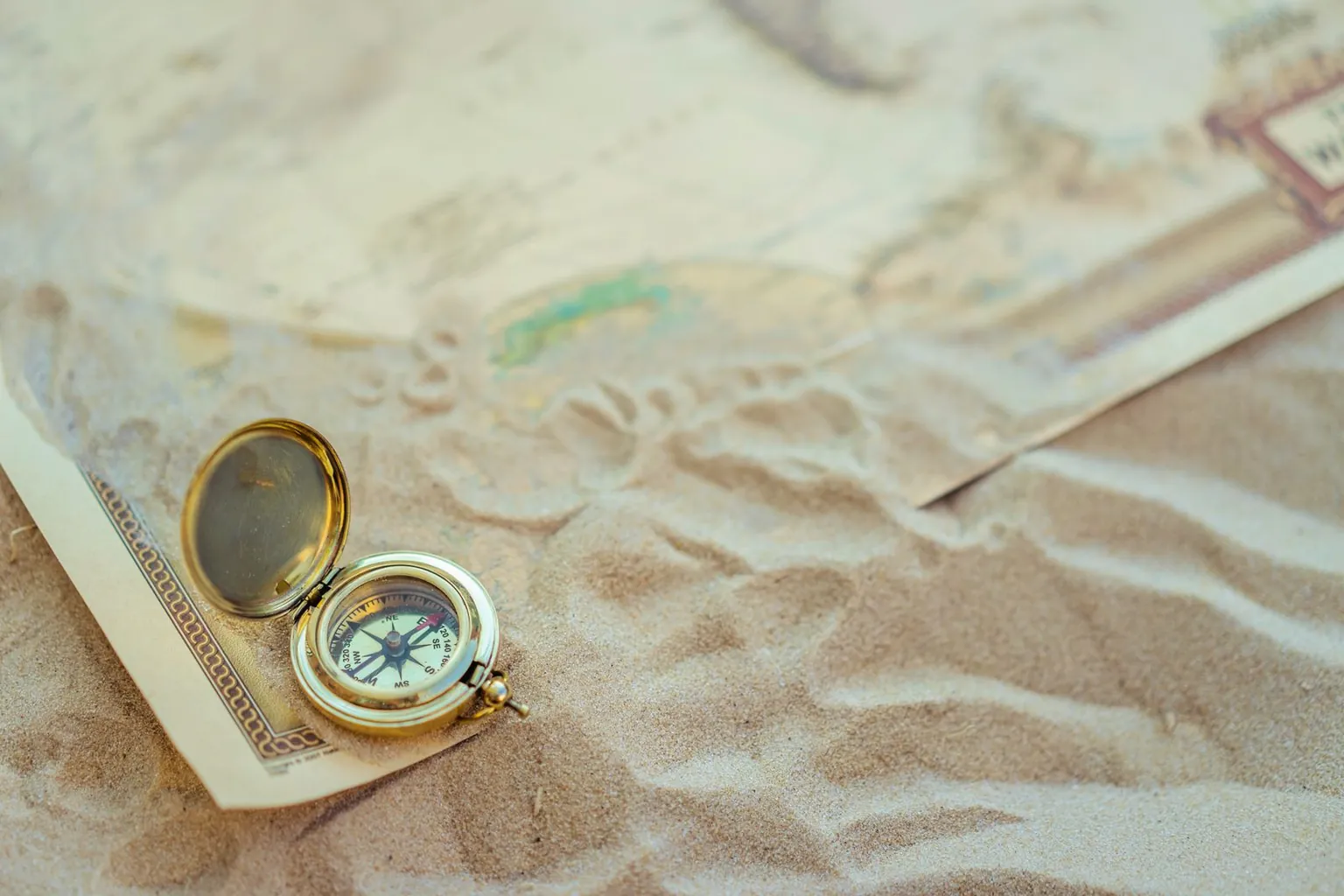 Une boussole ouverte posée sur une vieille carte et du sable.