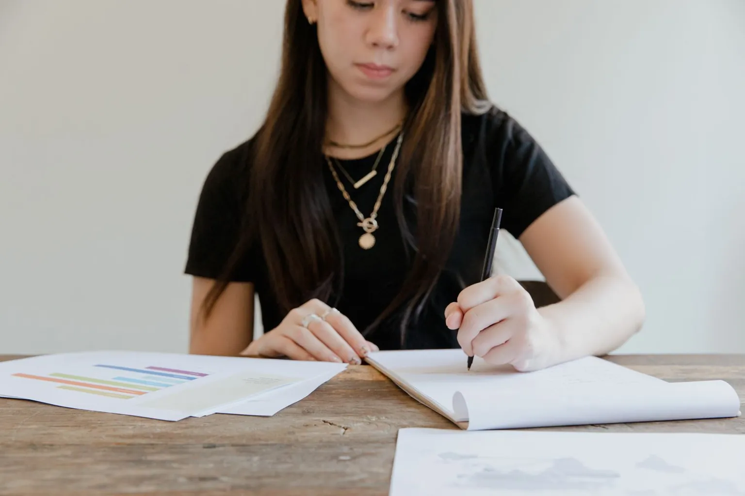 Une adolescente gauchère écrit sur un bloc-notes à une table en bois.
