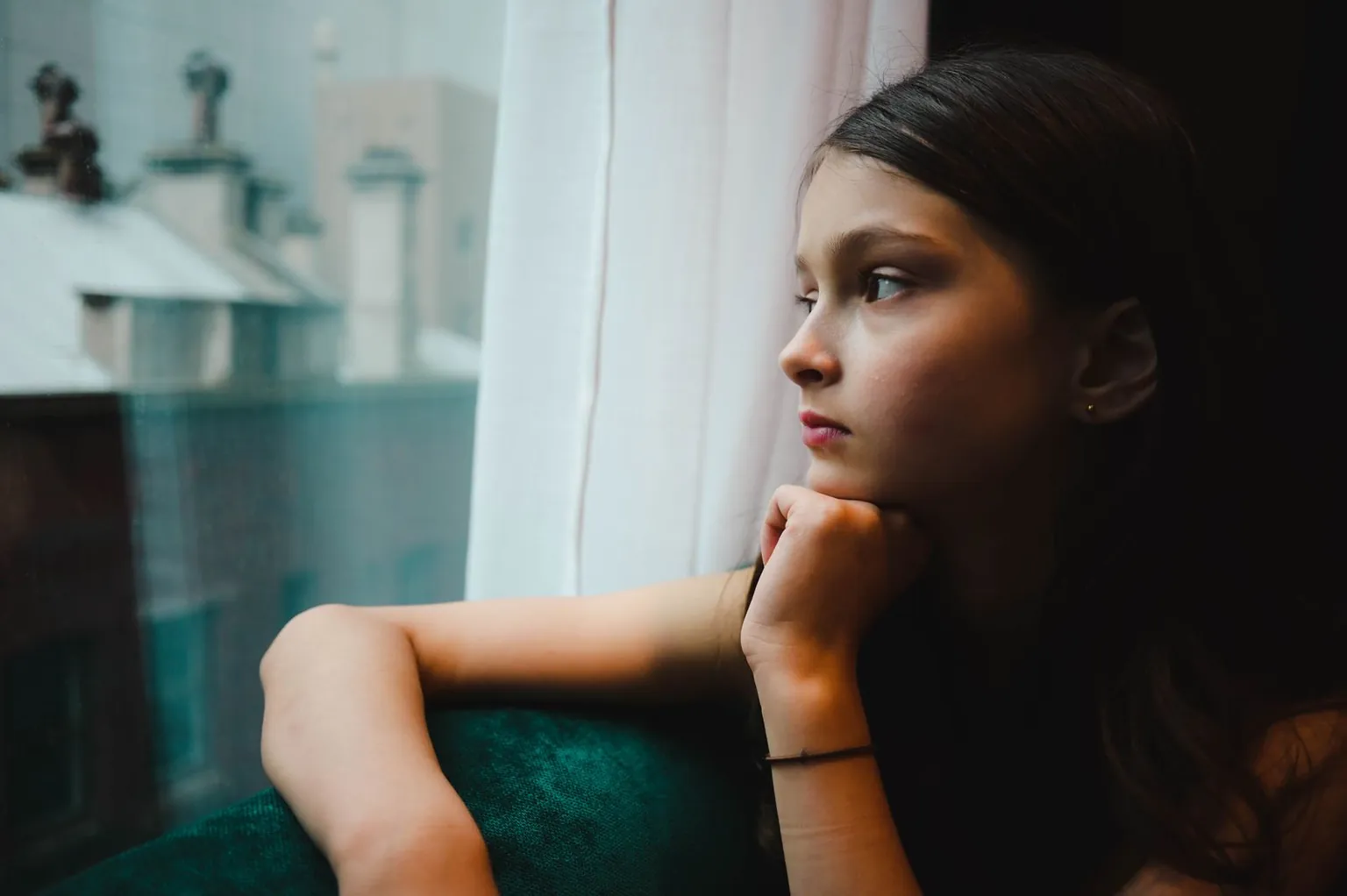 Une fille regarde par la fenêtre, le menton posé sur la main.