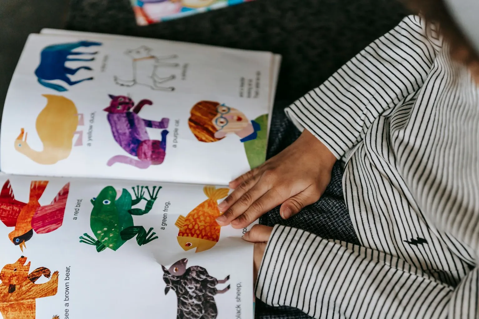 Une main d’enfant désigne les animaux d’un imagier ouvert.
