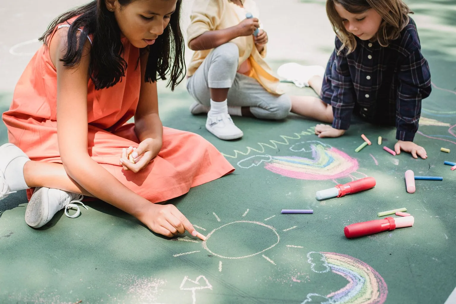 Des enfants dessinent à la craie sur le sol d’une cour.