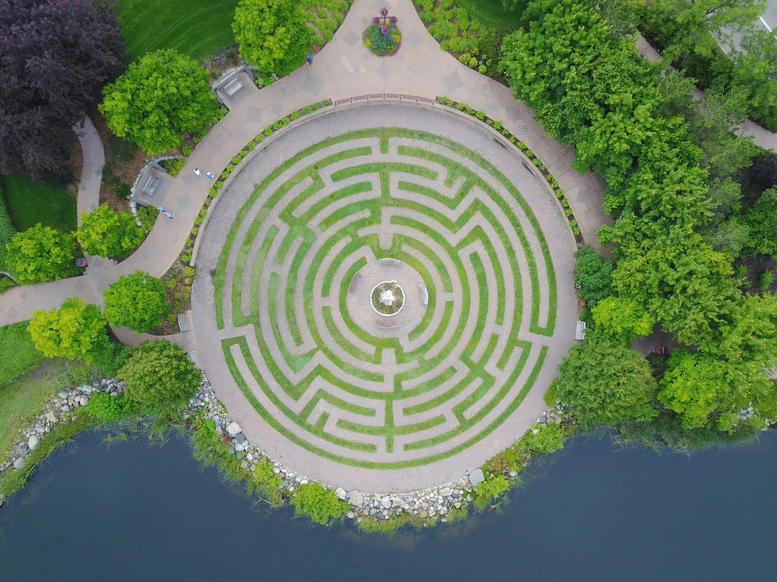 Un labyrinthe végétal circulaire vu du ciel, au bord de l’eau.