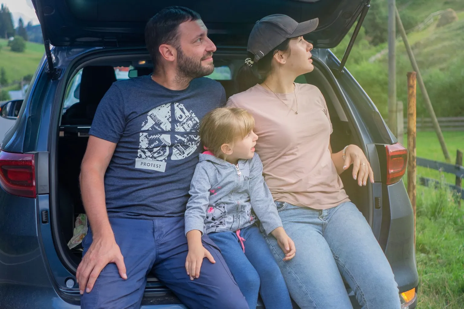 Une famille fait une pause assise dans le coffre ouvert de sa voiture.