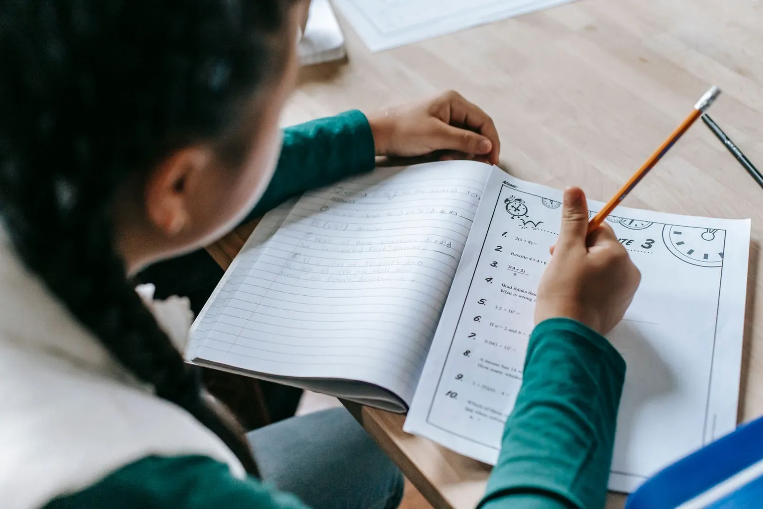 Une enfant écrit dans son cahier avec un crayon à papier.