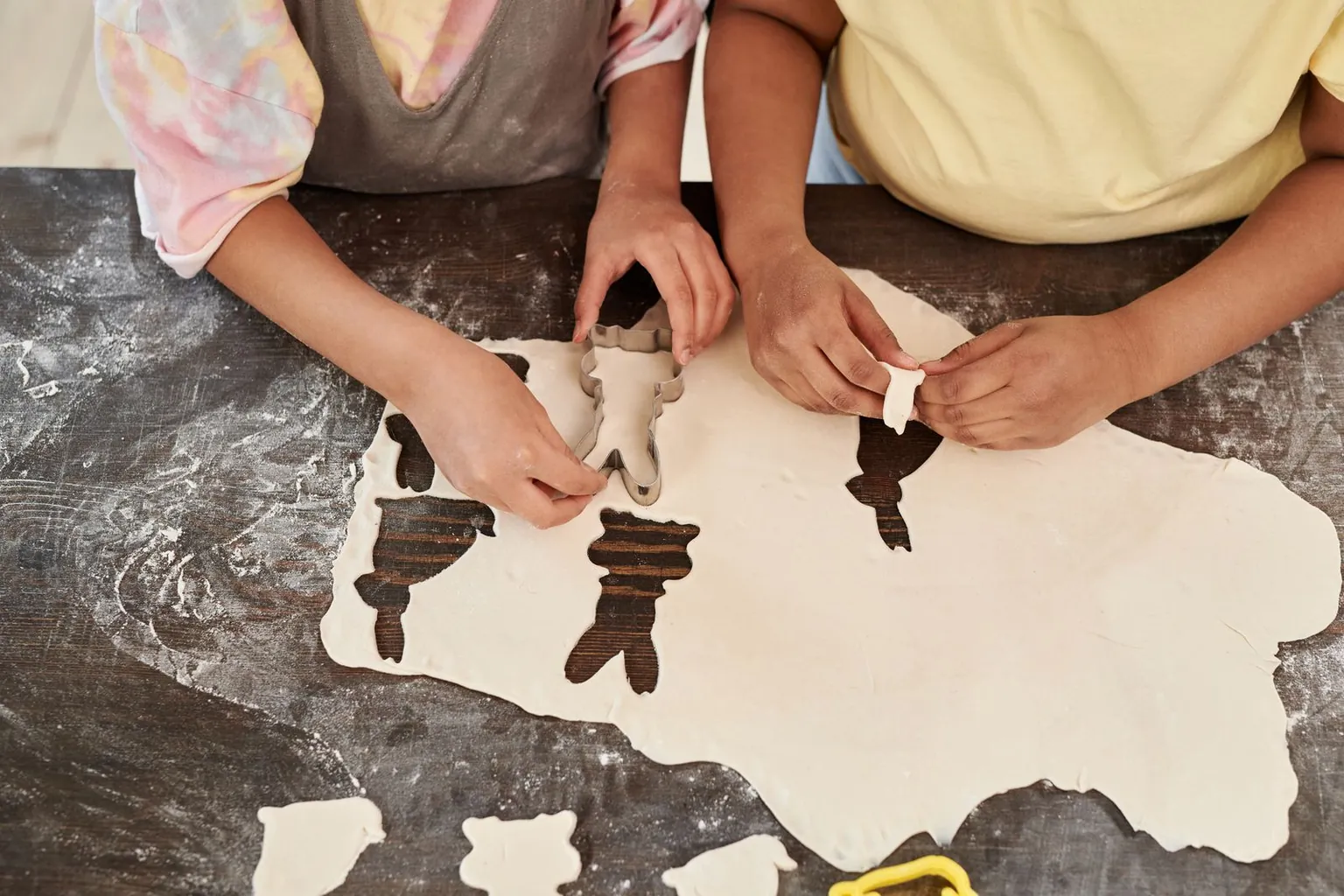 Des mains d’enfants découpent des formes dans une pâte étalée.