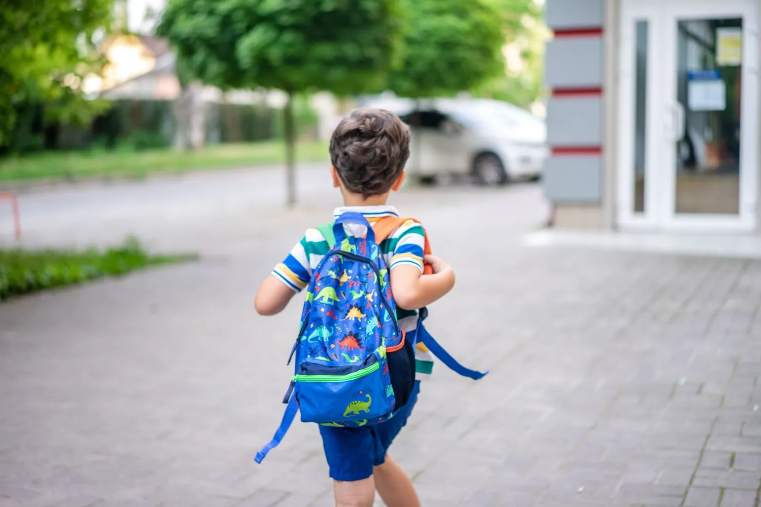 Un jeune garçon marche avec un cartable coloré sur le dos.