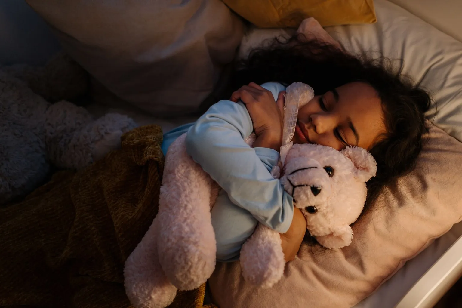 Une fillette dort en serrant une peluche dans son lit.