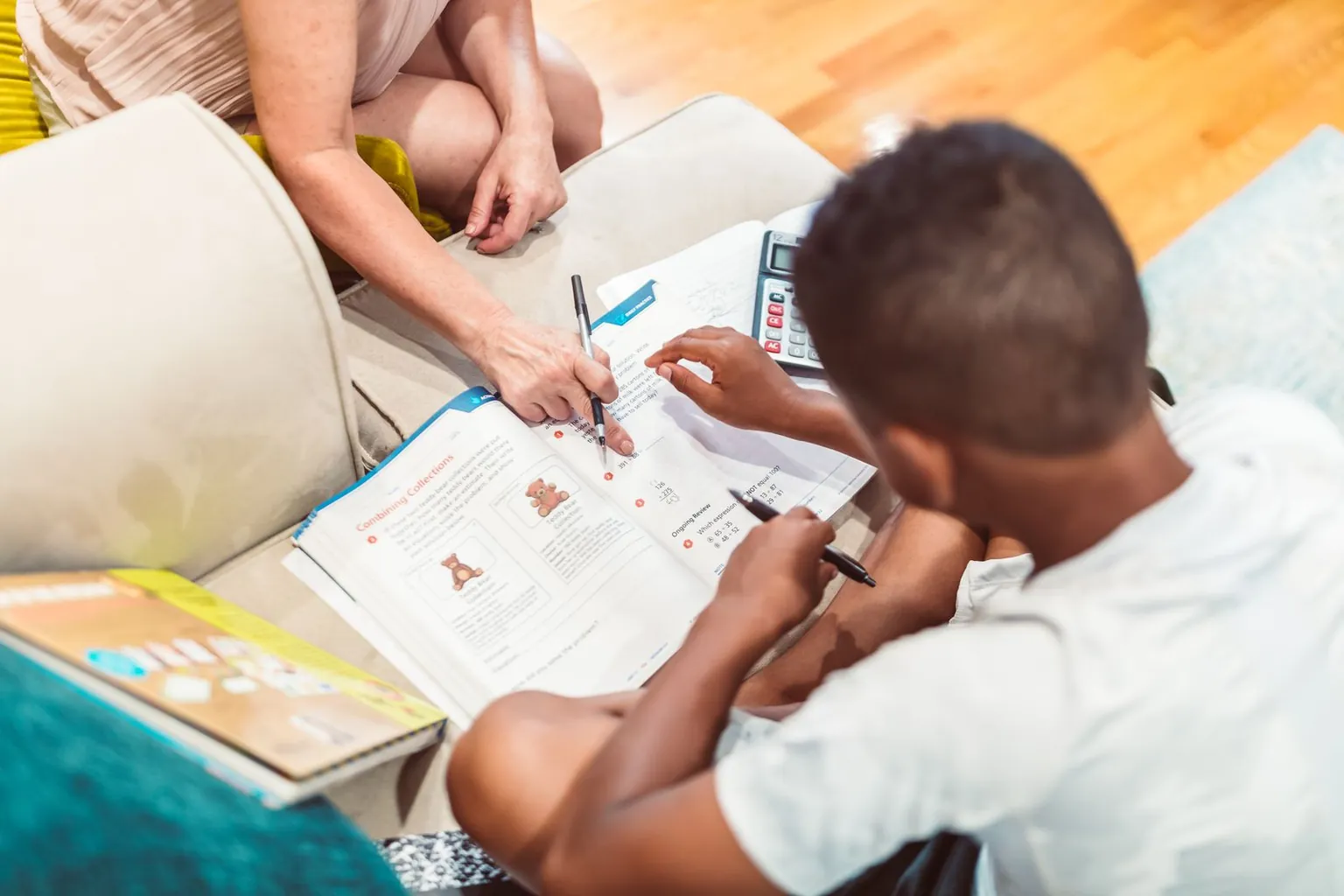 Un adulte aide un garçon à faire ses exercices de maths assis près du canapé.